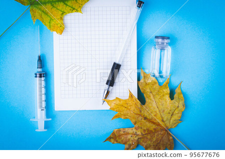 Syringe notebook and autumn leaves lie on blue desk of doctor in hospital. Syringe notebook and autumn leaves lie on blue desk of doctor in hospital. 95677676