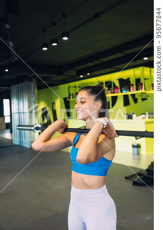 Strong young woman doing sit-ups with a barbell Strong young woman doing sit-ups with a barbell 95677844
