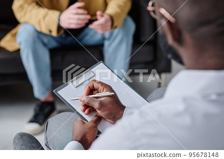 Close-up of psychotherapist making notes in patient card during conversation with patient at session Close-up of psychotherapist making notes in patient card during conversation with patient at session 95678148