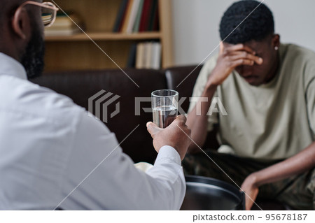 African psychotherapist giving glass of water to support patient at office during psychotherapy session African psychotherapist giving glass of water to support patient at office during psychotherapy session 95678187