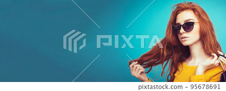 Shopping Concept - Close up Portrait young beautiful attractive redhair girl smiling looking at camera with shopping bag. Blue Pastel Background. Copy space Shopping Concept - Close up Portrait young beautiful attractive redhair girl smiling looking at camera with shopping bag. Blue Pastel Background. Copy space 95678691