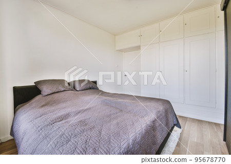 Home interior design of bedroom with bed and wooden wardrobe placed in corner near window in modern apartment 95678770