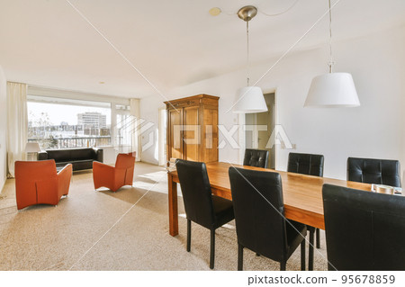 Comfortable chairs and wooden table placed under stylish lamps against wall with cupboard in dining room 95678859