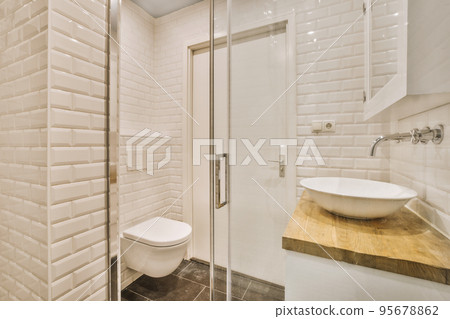 Flush toilet and shower cabin with glass partition and curtain located near sink and shelf with cosmetic products in washroom at home 95678862