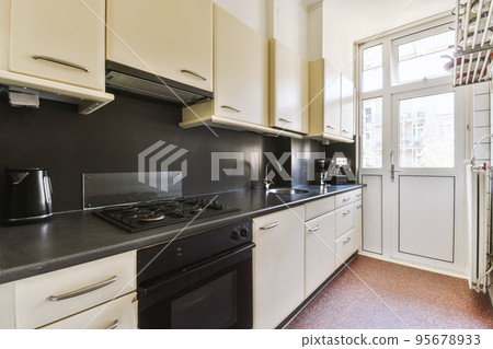 Fragment of interior of light narrow home kitchen with minimalist style white furniture with sink and stove 95678933