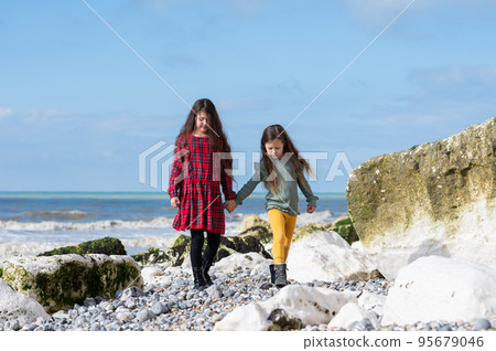 Two little girls in red tartan dress, green jumper and yellow leggings walking at Hope Gap beach near Cuckmere Haven located between Seaford and Eastbourne in East Sussex, British south coast 95679046
