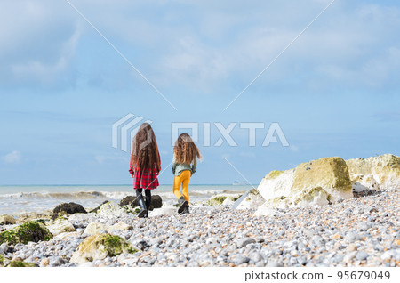 Back view of two little girls in red tartan dress, green jumper and yellow leggings walking at Hope Gap beach near Cuckmere Haven located between Seaford and Eastbourne in East Sussex, UK Back view of two little girls in red tartan dress, green jumper and yellow leggings walking at Hope Gap beach near Cuckmere Haven located between Seaford and Eastbourne in East Sussex, UK 95679049