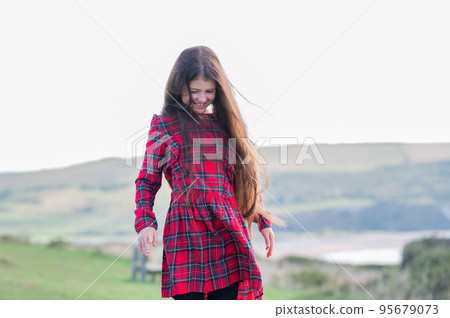 Little girl with long brown hair in red tartan dress standing on the grass, nature on the background, looking at Cuckmere beach in East Sussex, UK Little girl with long brown hair in red tartan dress standing on the grass, nature on the background, looking at Cuckmere beach in East Sussex, UK 95679073