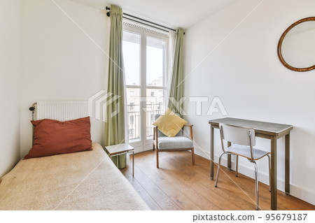 Minimalist interior design of small bedroom with soft bed placed in corner and table with shelves,armchair with lamp illumination 95679187