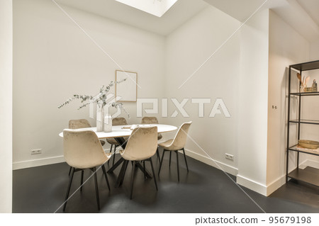 Modern minimalist style interior design of studio apartment with open white kitchen and dining zone with table and chairs illuminated by loft style lamp 95679198