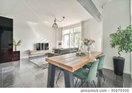Table with chairs and flowers located near lounge area and kitchen in spacious room of contemporary apartment 95679308
