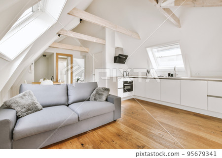 Contemporary minimalist style interior design of light studio apartment with wooden table and chairs in dining zone between open kitchen and living room with white walls and parquet floor 95679341