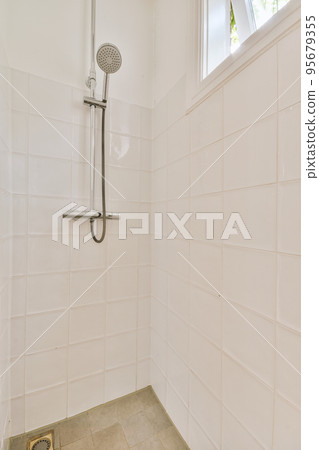 Shower faucets attached to tiled wall near glass partition and ornamental curtail in washroom at home 95679355