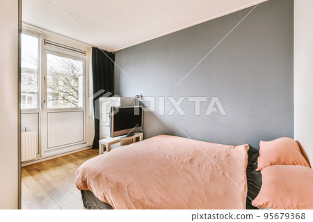 Minimalist interior design of small bedroom with soft bed placed in corner and wooden wardrobe and shelves with lamp illumination Minimalist interior design of small bedroom with soft bed placed in corner and wooden wardrobe and shelves with lamp illumination 95679368