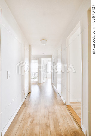 Light narrow hallway with many doors in white walls and glowing lamp over lumber floor Light narrow hallway with many doors in white walls and glowing lamp over lumber floor 95679427