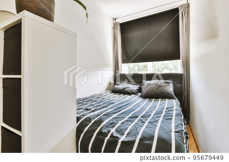 Home interior design of bedroom with bed and wooden wardrobe placed in corner near window in modern apartment Home interior design of bedroom with bed and wooden wardrobe placed in corner near window in modern apartment 95679449