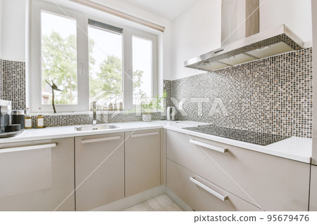 Fragment of interior of light narrow home kitchen with minimalist style white furniture with sink and stove Fragment of interior of light narrow home kitchen with minimalist style white furniture with sink and stove 95679476