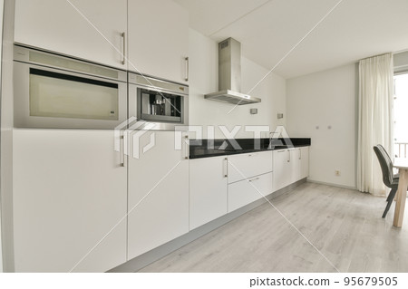 Table with chairs and flowers located near lounge area and kitchen in spacious room of contemporary apartment 95679505