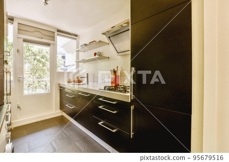 Fragment of interior of light narrow home kitchen with minimalist style black furniture with sink and stove Fragment of interior of light narrow home kitchen with minimalist style black furniture with sink and stove 95679516