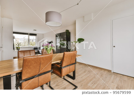Shabby wooden table with chairs and vase located near comfortable couch against light walls with decorations and TV in modern apartment 95679599