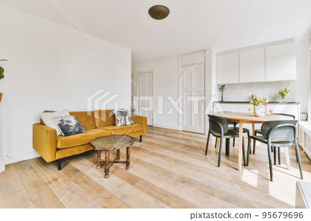 Contemporary minimalist style interior design of light studio apartment with wooden table and chairs in dining zone between open kitchen and living room with white walls and parquet floor Contemporary minimalist style interior design of light studio apartment with wooden table and chairs in dining zone between open kitchen and living room with white walls and parquet floor 95679696
