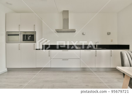 Table with chairs and flowers located near lounge area and kitchen in spacious room of contemporary apartment Table with chairs and flowers located near lounge area and kitchen in spacious room of contemporary apartment 95679721