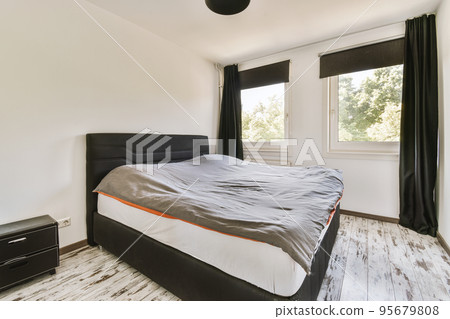 Home interior design of bedroom with bed and wooden wardrobe placed in corner near window in modern apartment 95679808