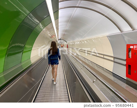 A beautiful girl walks along the travolator in the subway tunnel to go to another underground station. View from the back A beautiful girl walks along the travolator in the subway tunnel to go to another underground station. View from the back 95680441