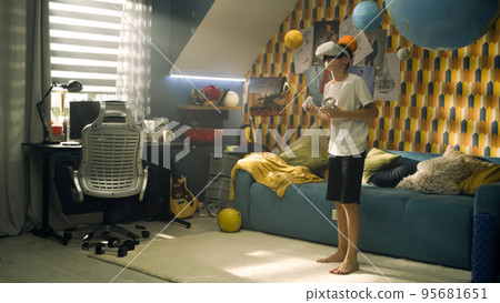A teenage boy plays a fighting game using virtual reality headset and joysticks A teenage boy plays a fighting game using virtual reality headset and joysticks 95681651