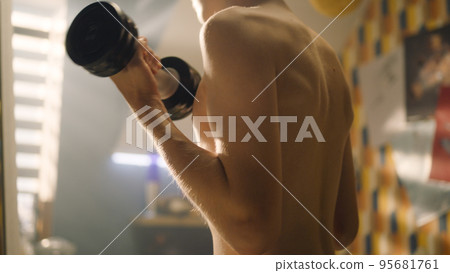 Closeup bare upper body of young muscular school boy do dumbbell curls in room 95681761