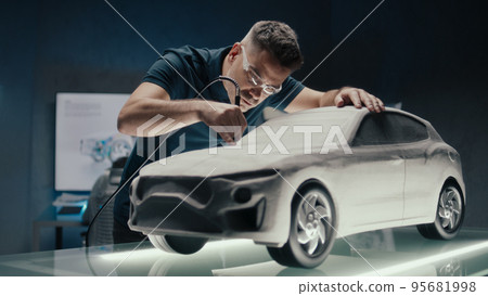 Senior car designer works on prototype car clay sculpture using a rotating tool 95681998