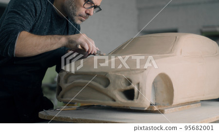 Car designer works on the model of car using shaping tools to smooth out bonnet Car designer works on the model of car using shaping tools to smooth out bonnet 95682001