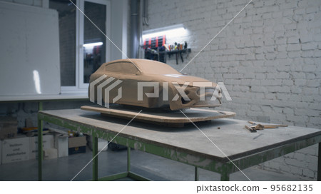 Unfinished sculpture of prototype car placed on a wooden table with laying tools 95682135