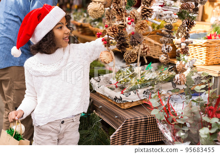 Portrait of joyful small girl in hat choosing Christmas toys Portrait of joyful small girl in hat choosing Christmas toys 95683455