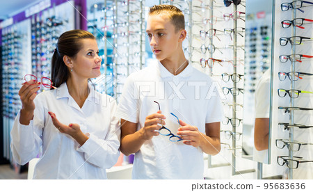 Optician consulting teenager in optical store 95683636