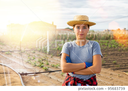 Young female horticulturist standing in farm field with irrigation system 95683739