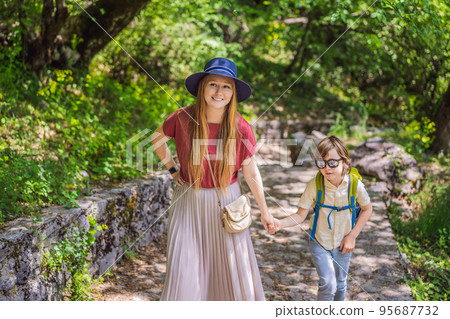 Mother and son tourists climb the mountain to the Ostrog temple. Monastery of Ostrog, Serbian Orthodox Church situated against a vertical background, high up in the large rock of Ostroska Greda Mother and son tourists climb the mountain to the Ostrog temple. Monastery of Ostrog, Serbian Orthodox Church situated against a vertical background, high up in the large rock of Ostroska Greda 95687732