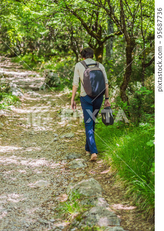 Man tourist climb barefoot the mountain to the Ostrog. It is a tradition to climb barefoot. Monastery of Ostrog, Serbian Orthodox Church situated against a vertical background, high up in the large Man tourist climb barefoot the mountain to the Ostrog. It is a tradition to climb barefoot. Monastery of Ostrog, Serbian Orthodox Church situated against a vertical background, high up in the large 95687736