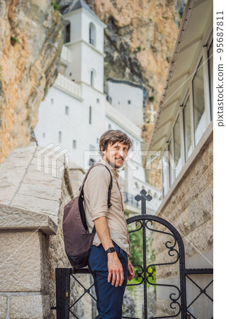 Man tourist in Monastery of Ostrog, Serbian Orthodox Church situated against a vertical background, high up in the large rock of Ostroska Greda, Montenegro. Dedicated to Saint Basil of Ostrog Man tourist in Monastery of Ostrog, Serbian Orthodox Church situated against a vertical background, high up in the large rock of Ostroska Greda, Montenegro. Dedicated to Saint Basil of Ostrog 95687811