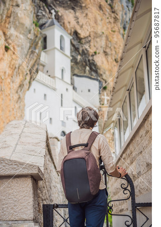 Man tourist in Monastery of Ostrog, Serbian Orthodox Church situated against a vertical background, high up in the large rock of Ostroska Greda, Montenegro. Dedicated to Saint Basil of Ostrog 95687817