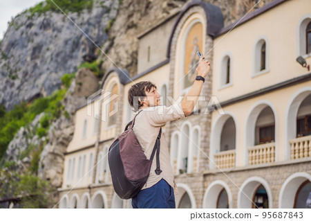 Man tourist in Monastery of Ostrog, Serbian Orthodox Church situated against a vertical background, high up in the large rock of Ostroska Greda, Montenegro. Dedicated to Saint Basil of Ostrog 95687843