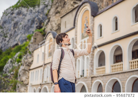 Man tourist in Monastery of Ostrog, Serbian Orthodox Church situated against a vertical background, high up in the large rock of Ostroska Greda, Montenegro. Dedicated to Saint Basil of Ostrog 95687872