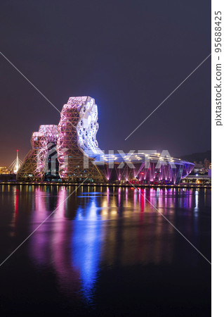 Night view of Kaohsiung Music Center with a view from Love River. The white hexagonal building structure on the riverbank in Kaohsiung, Taiwan. 95688425
