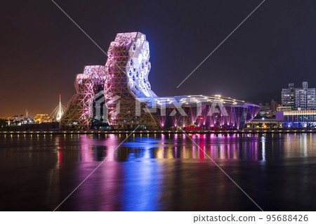 Night view of Kaohsiung Music Center with a view from Love River. The white hexagonal building structure on the riverbank in Kaohsiung, Taiwan. 95688426