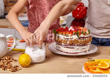 Little friends are making a cake together at a kitchen against a white wall with shelves on it. Little friends are making a cake together at a kitchen against a white wall with shelves on it. 95688859