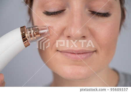 Caucasian woman uses a vacuum pore cleaner at home. Caucasian woman uses a vacuum pore cleaner at home. 95689337