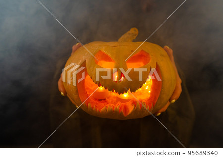 The witch is holding a pumpkin jack about a lantern glowing in the dark. Halloween. The witch is holding a pumpkin jack about a lantern glowing in the dark. Halloween. 95689340