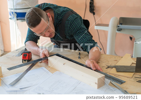 Carpenter measures wooden planks in the workshop. 95689521