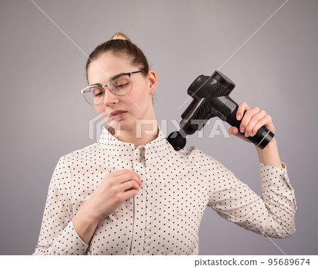 A caucasian woman uses a massager gun for pain in the muscles of her back and shoulders. A caucasian woman uses a massager gun for pain in the muscles of her back and shoulders. 95689674
