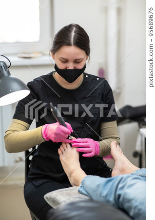 The pedicure master processes the client's foot using an apparatus with an abrasive disc. 95689676